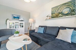 A modern living room with a grey sofa, a white coffee table, and a painting of a landscape. - Apartment 'Ferienwohnung Ankerleicht' with Shared Terrace, Shared Garden and Wi-Fi (Steinbergkirche)