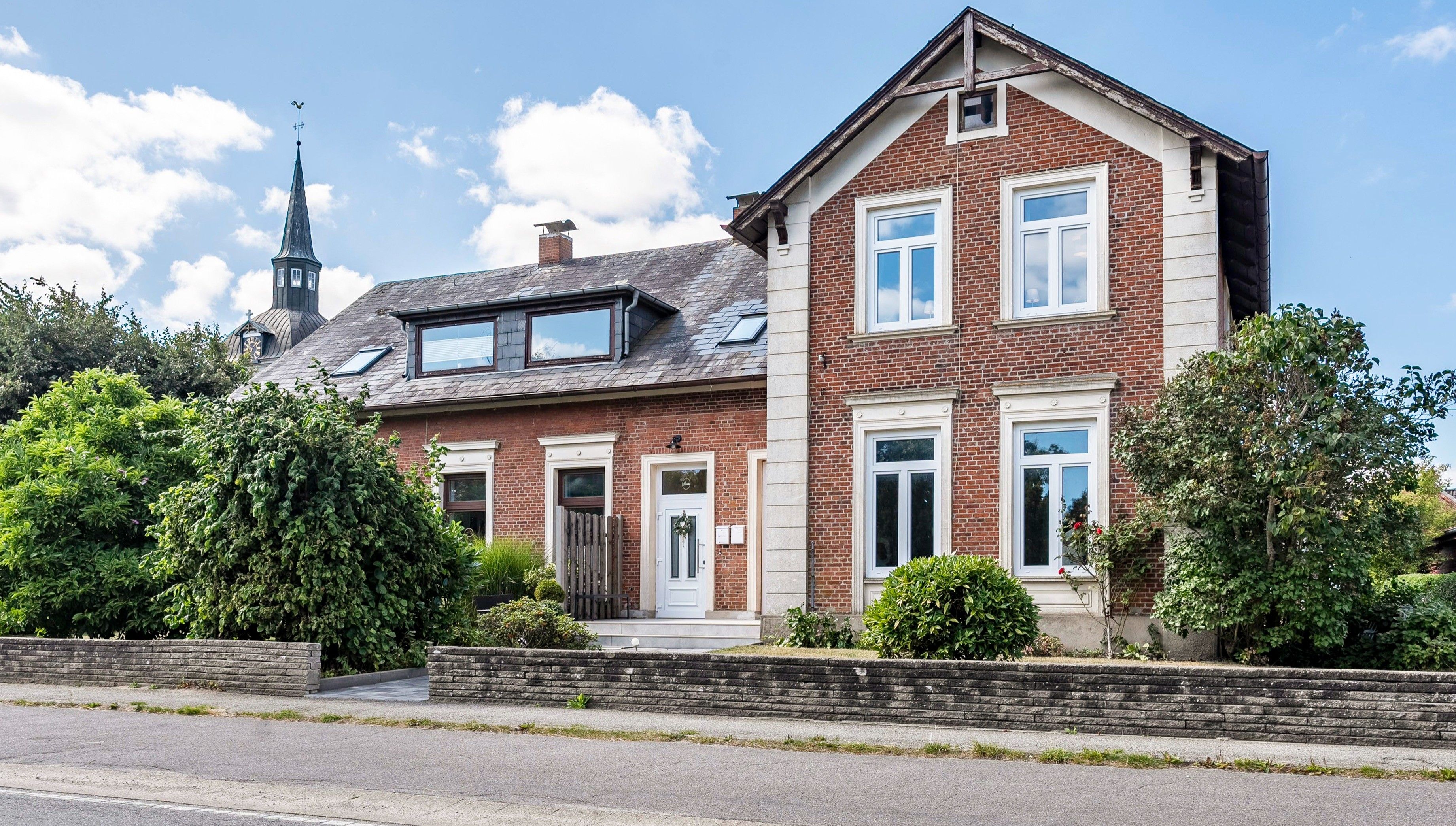 Ett tvåvåningshus byggt av tegel med ett sadeltak, en synlig skorsten och ett litet garage som är sammanbyggt med huset.