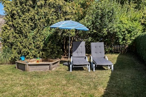 A garden with two lounge chairs, a wooden sandbox, and a blue-striped umbrella. - Apartment 'Ferienwohnung Ankerleicht' with Shared Terrace, Shared Garden and Wi-Fi (Steinbergkirche)