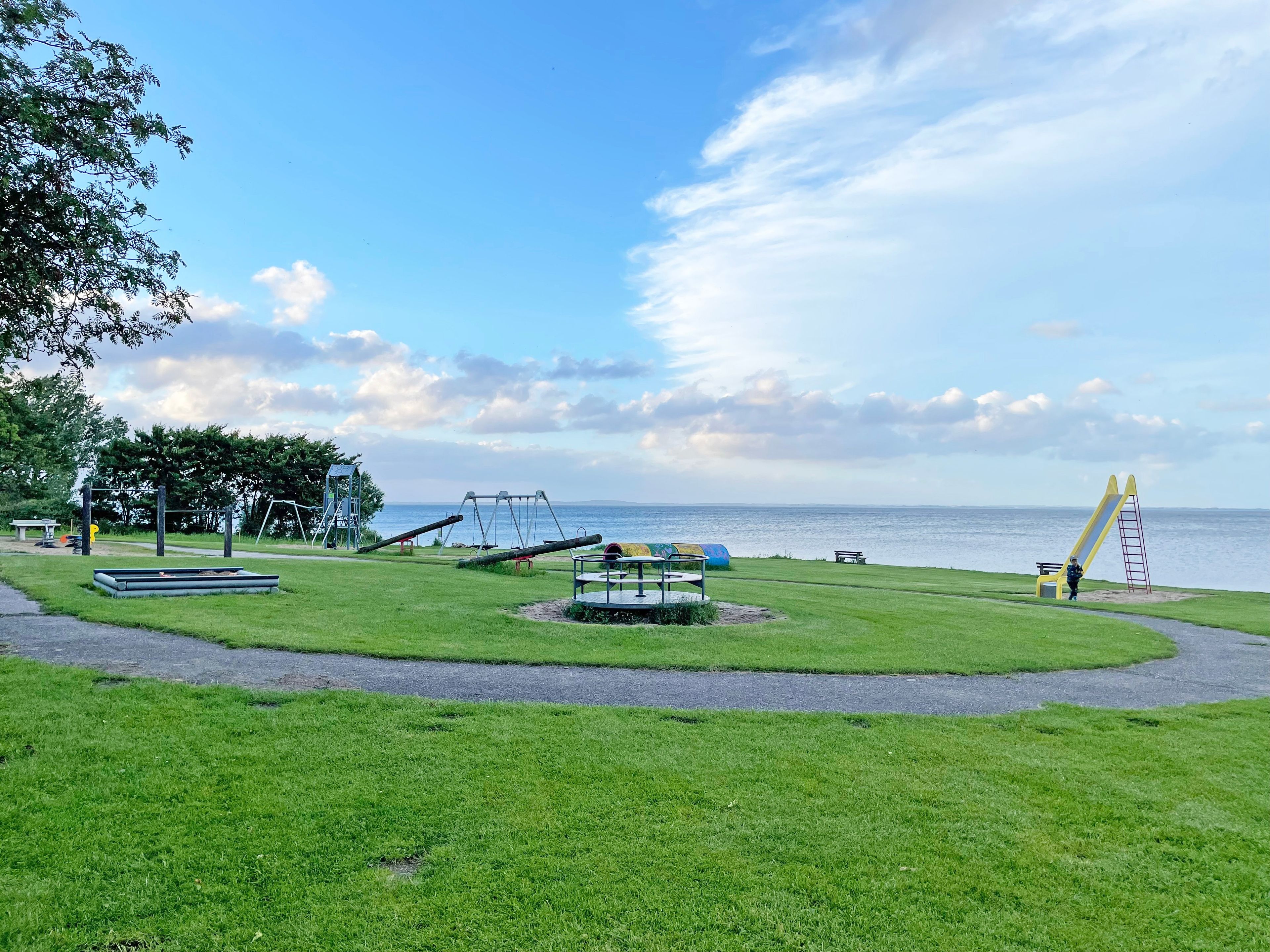 En park med lekutrustning, en bänk och utsikt över havet.