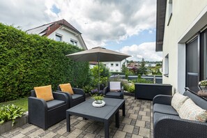 Patio esterno con mobili in vimini, un tavolo e un ombrellone.