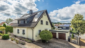 Una casa con techo inclinado, paneles solares, garaje y entrada pavimentada.