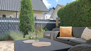 Un patio con mobiliario exterior, una mesa con dos individuales y un seto.