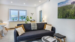 A modern living room with a grey sofa, a round coffee table, and a large window with a view of a field. - Apartment 'Reinbold' with Private Terrace, Private Garden and Wi-Fi (Niedereschach)