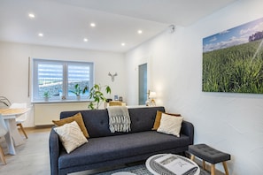 Un salón moderno con un sofá gris, una mesa redonda de centro y un ventanal con vistas a un campo.