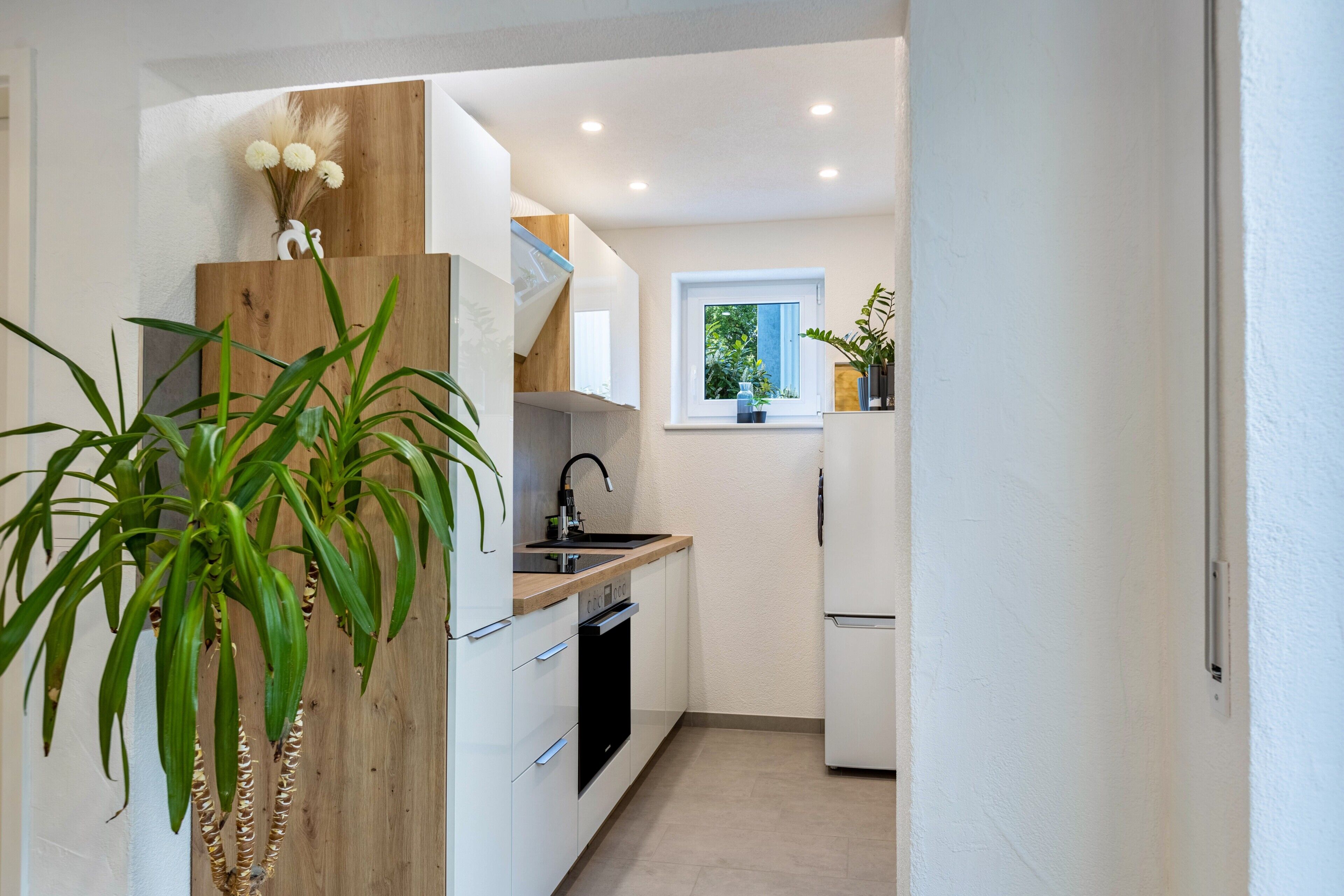 Una cocina moderna con armarios blancos, una pared de acento de madera, un horno empotrado y una ventana con vistas a la vegetación.