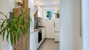 A modern kitchen with white cabinets, a wooden accent wall, a built-in oven, and a window with a view of greenery. - Apartment 'Reinbold' with Private Terrace, Private Garden and Wi-Fi (Niedereschach)