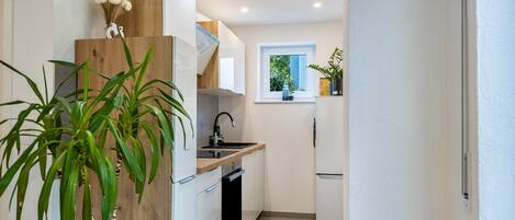 Una cocina moderna con armarios blancos, una pared de acento de madera, un horno empotrado y una ventana con vistas a la vegetación.
