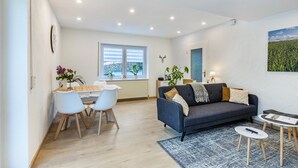 A modern living room with a sofa, coffee table, and dining area. - Apartment 'Reinbold' with Private Terrace, Private Garden and Wi-Fi (Niedereschach)