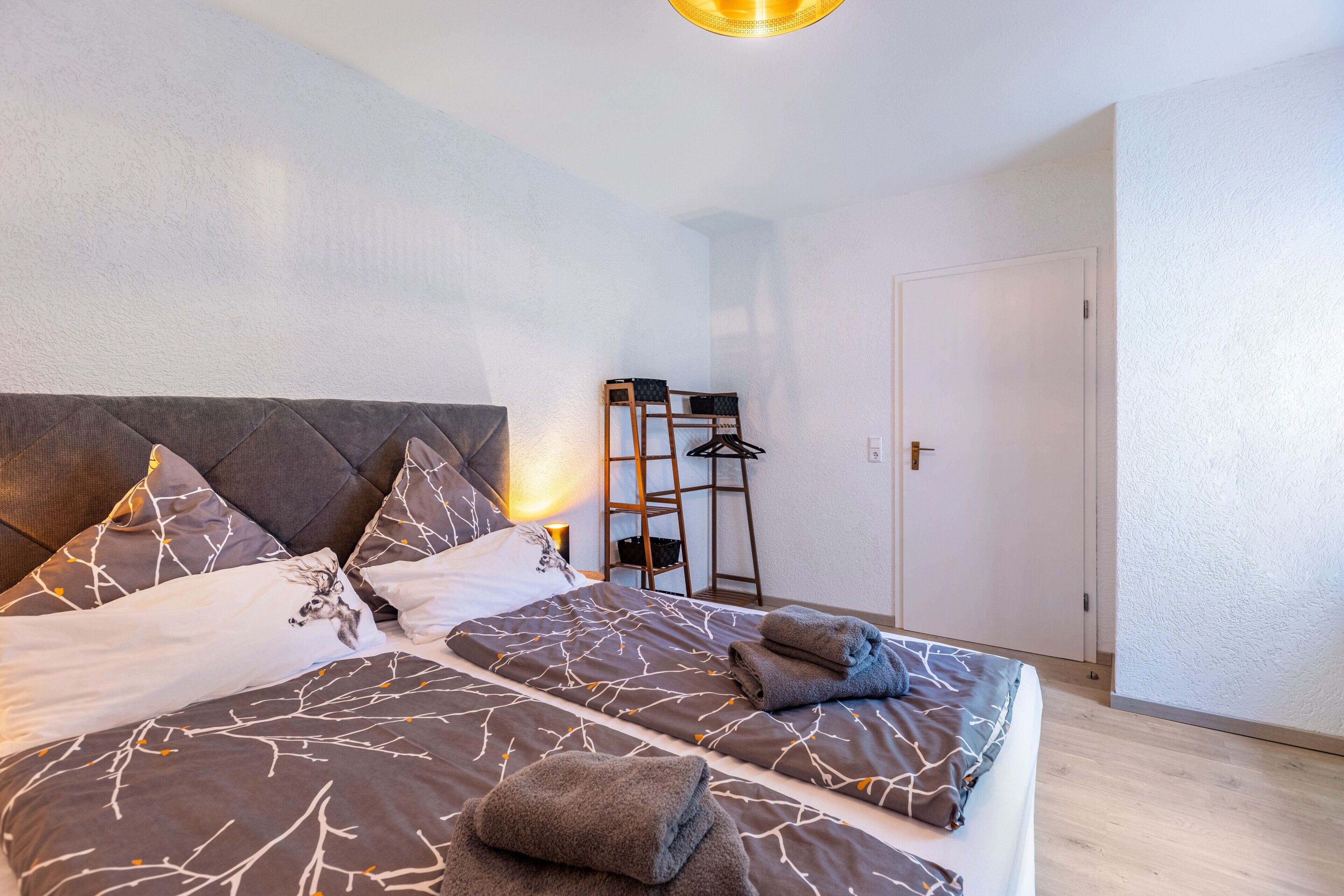 A bedroom with a bed, pillows, a bedside table, a hanging rack, and a door.