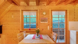 Une cabane en bois avec une table à manger, des chaises, une horloge et une fenêtre donnant sur un paysage verdoyant.