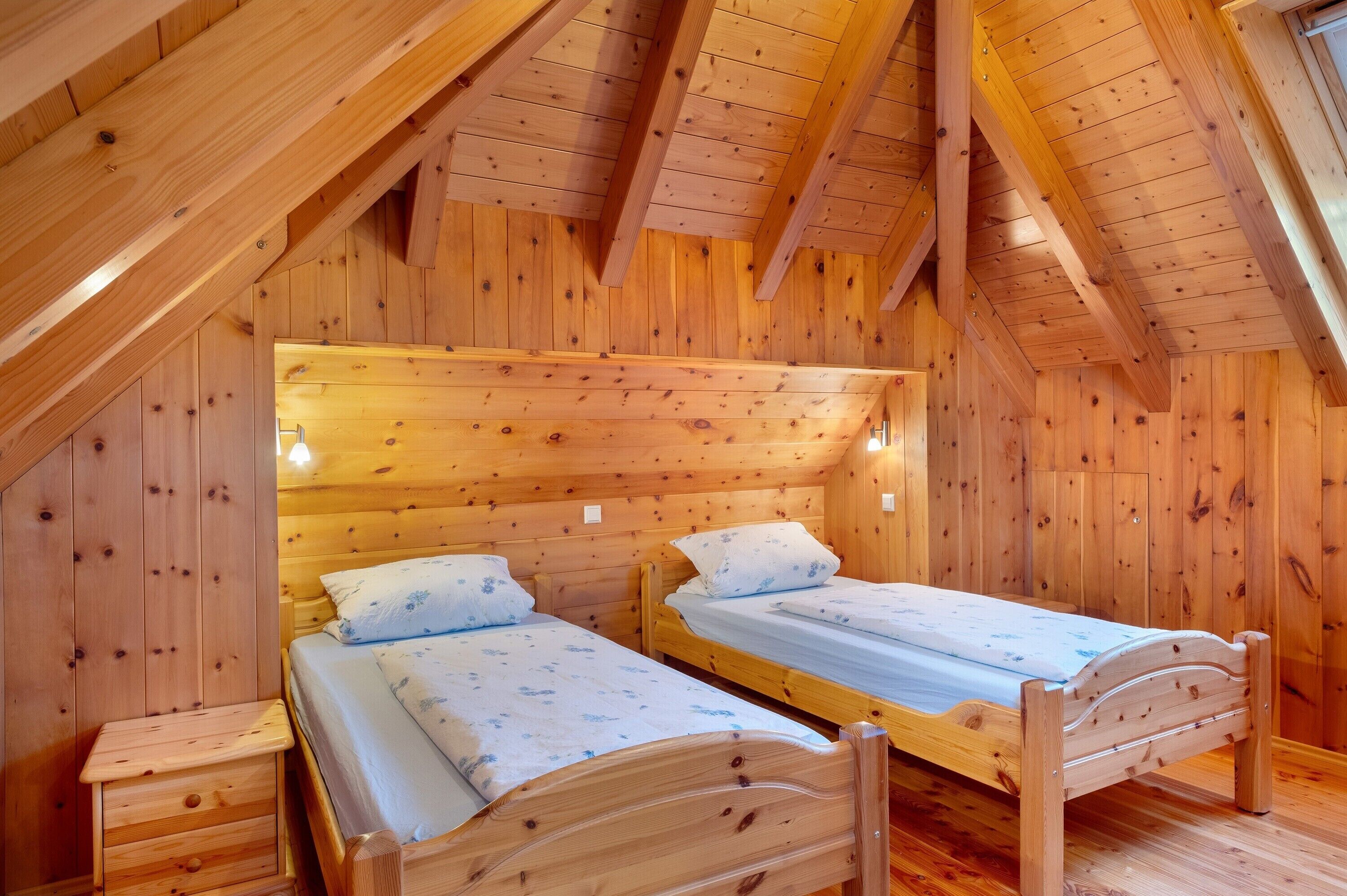 A wooden cabin with two wooden beds, a small wooden nightstand, and a sloped ceiling.