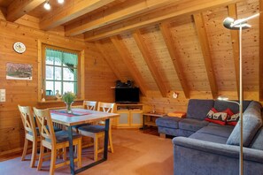 En mysig stuga i trä med ett matområde, en soffa, en TV och en takfläkt.