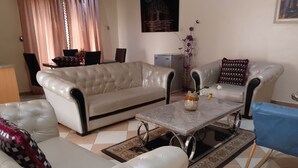 Un salon avec un canapé beige, un canapé blanc, une table basse et un fauteuil bleu.