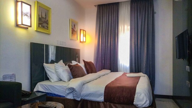 Une chambre d’hôtel avec un lit, un bureau et une chaise, une télévision et une fenêtre avec des rideaux.