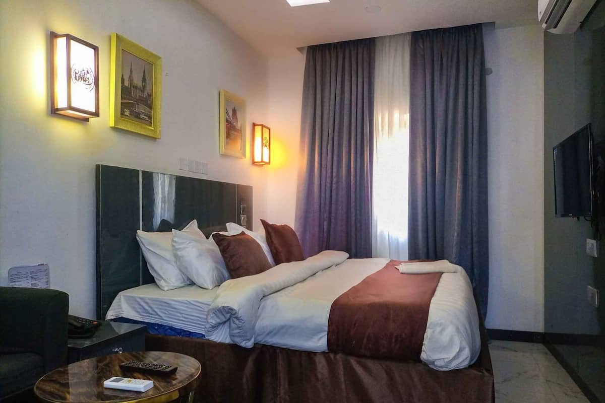 Une chambre d’hôtel avec un lit, un bureau et une chaise, une télévision et une fenêtre avec des rideaux.