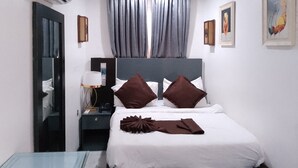 Une chambre d’hôtel avec un lit, une table de chevet, une lampe, un miroir et une fenêtre avec des rideaux.