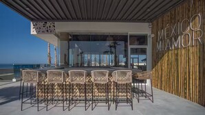 Un espace extérieur aménagé avec des chaises en osier et une cloison en verre, donnant sur une plage.