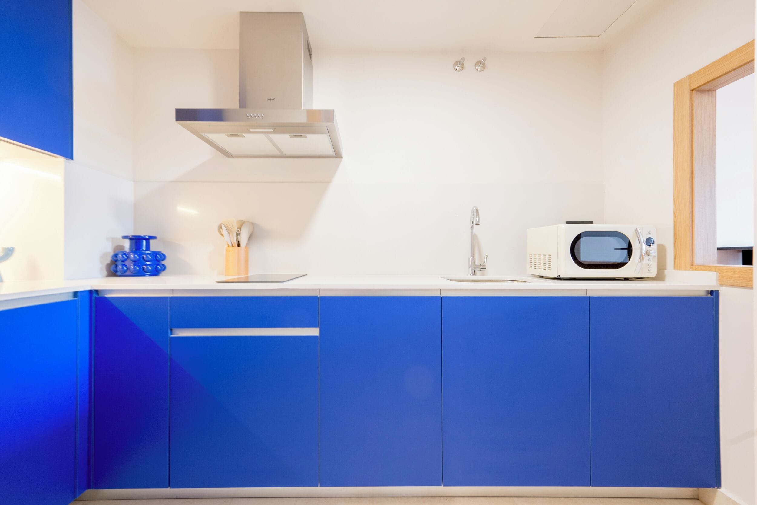 A modern kitchen with blue cabinets, a stainless steel range hood, a microwave, and a sink.