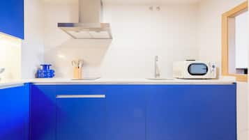 A modern kitchen with blue cabinets, a stainless steel range hood, a microwave, and a sink.