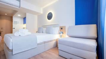 Una habitación de hotel moderna con dos camas, una mesita de noche, una lámpara y un ventanal grande con cortinas azules.
