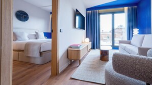 Quarto de hotel moderno com cama, sofá, televisão e varanda com cortinas azuis.