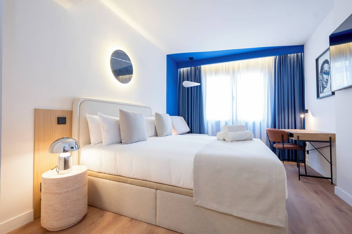 A modern hotel room with a large bed, a desk, and a round wall-mounted light.