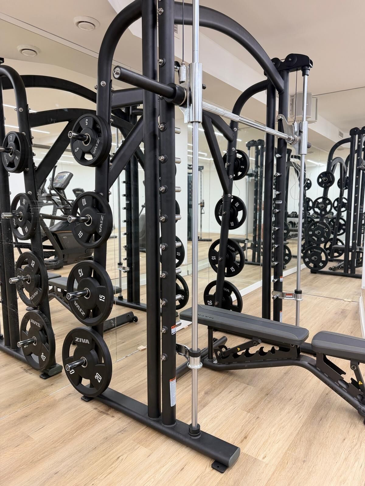 Un gimnasio con equipo de levantamiento de pesas, bancos y un espejo grande.