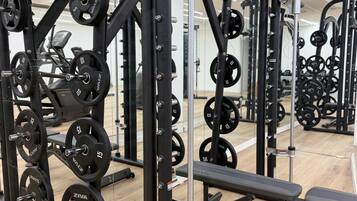 Un gimnasio con equipo de levantamiento de pesas, bancos y un espejo grande.