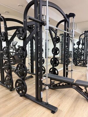 A gym with weightlifting equipment, benches, and a mirrored wall. - Iconic Suites (Madrid)