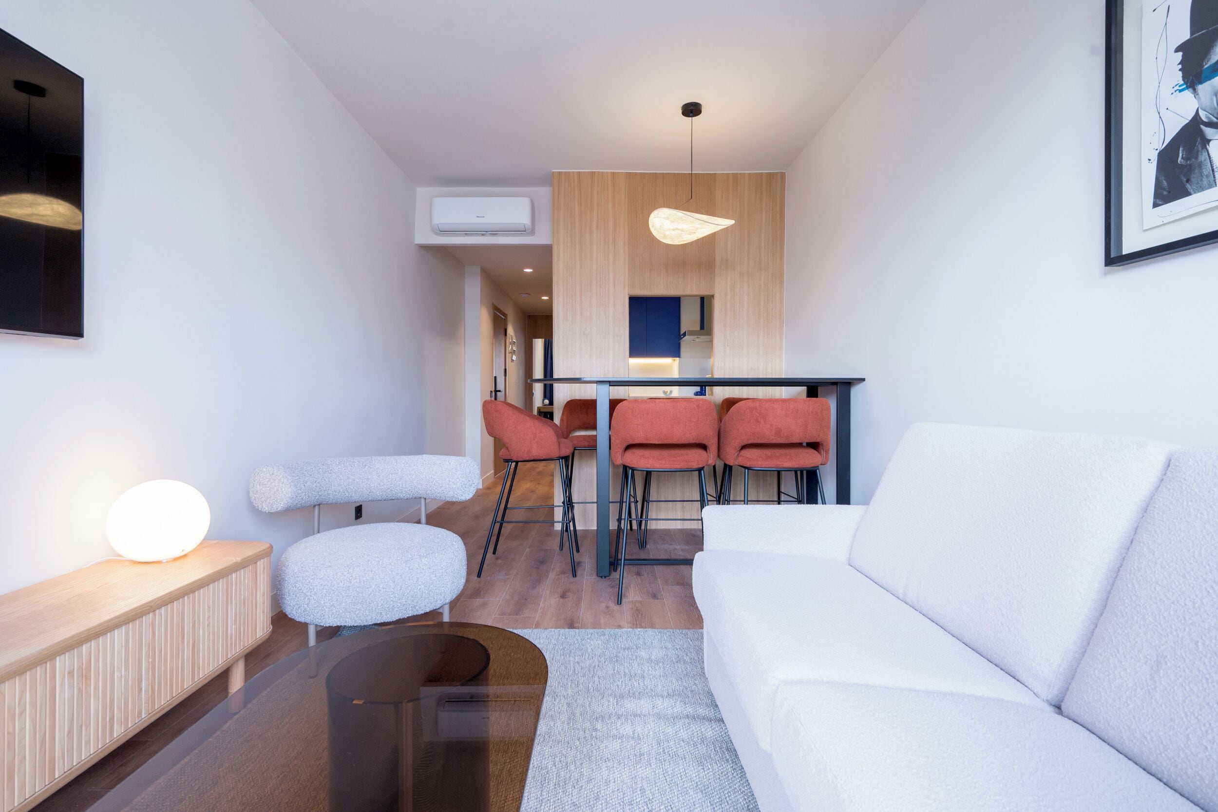 Una sala de estar moderna con un sofá blanco, una mesa de centro redonda y un comedor con sillas rojas y una mesa de madera.
