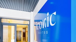 Entrada de hotel com design moderno, combinando um esquema de cores azul e branco e um letreiro com 'Iconic Suites'.