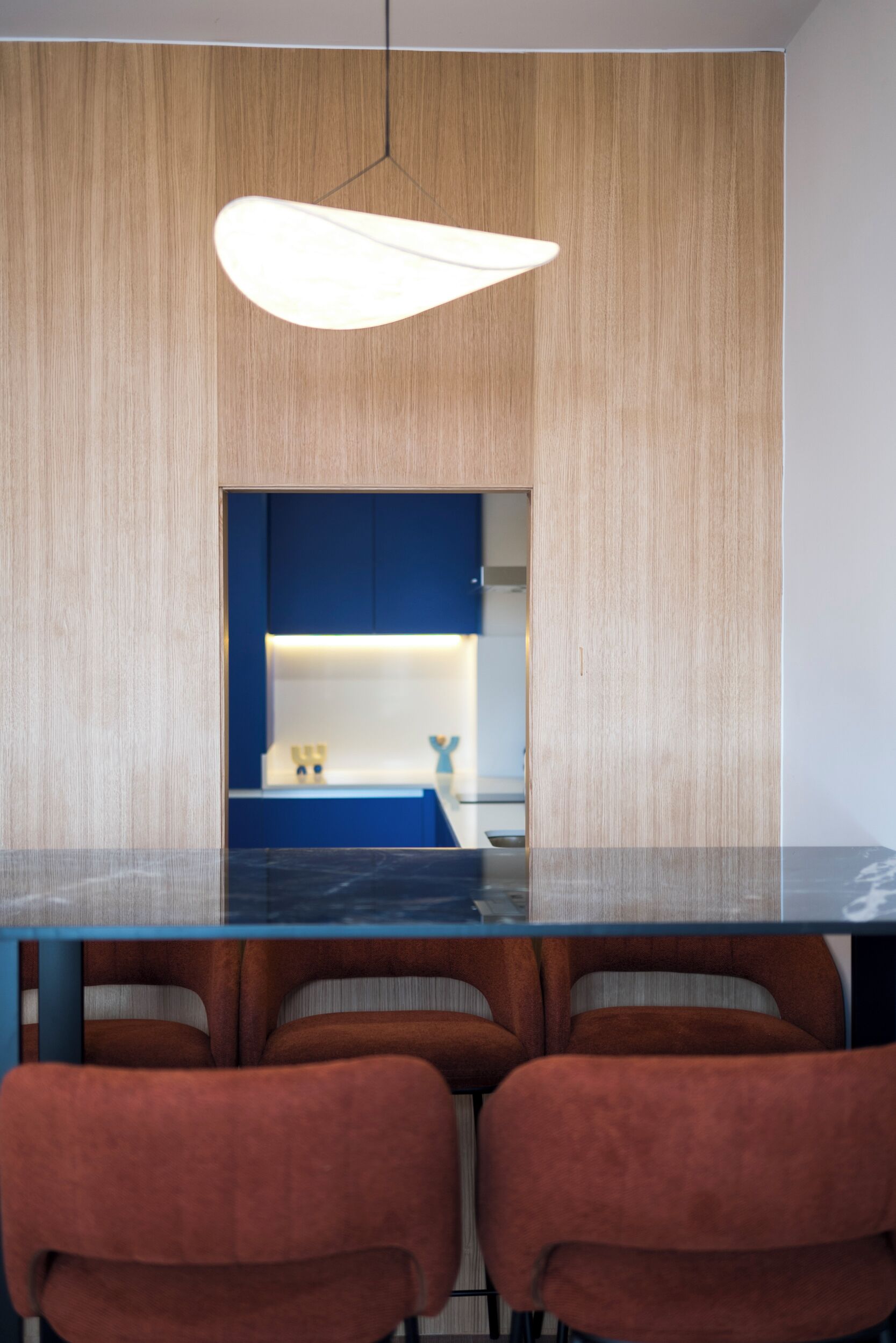A modern dining area with a dark marble table, brown upholstered chairs, and a blue accent wall.