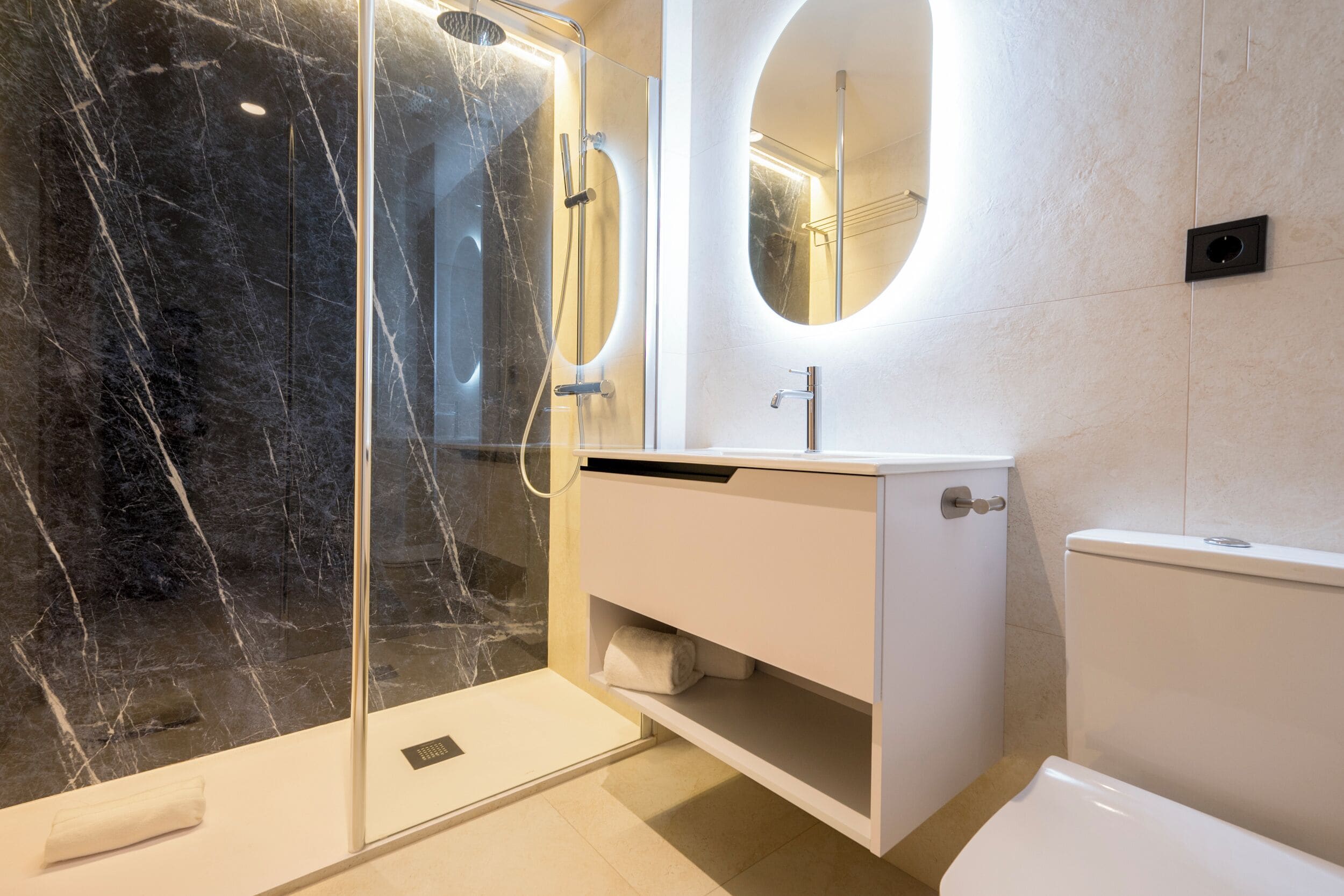Un baño moderno con ducha de vidrio, tocador blanco y un inodoro.