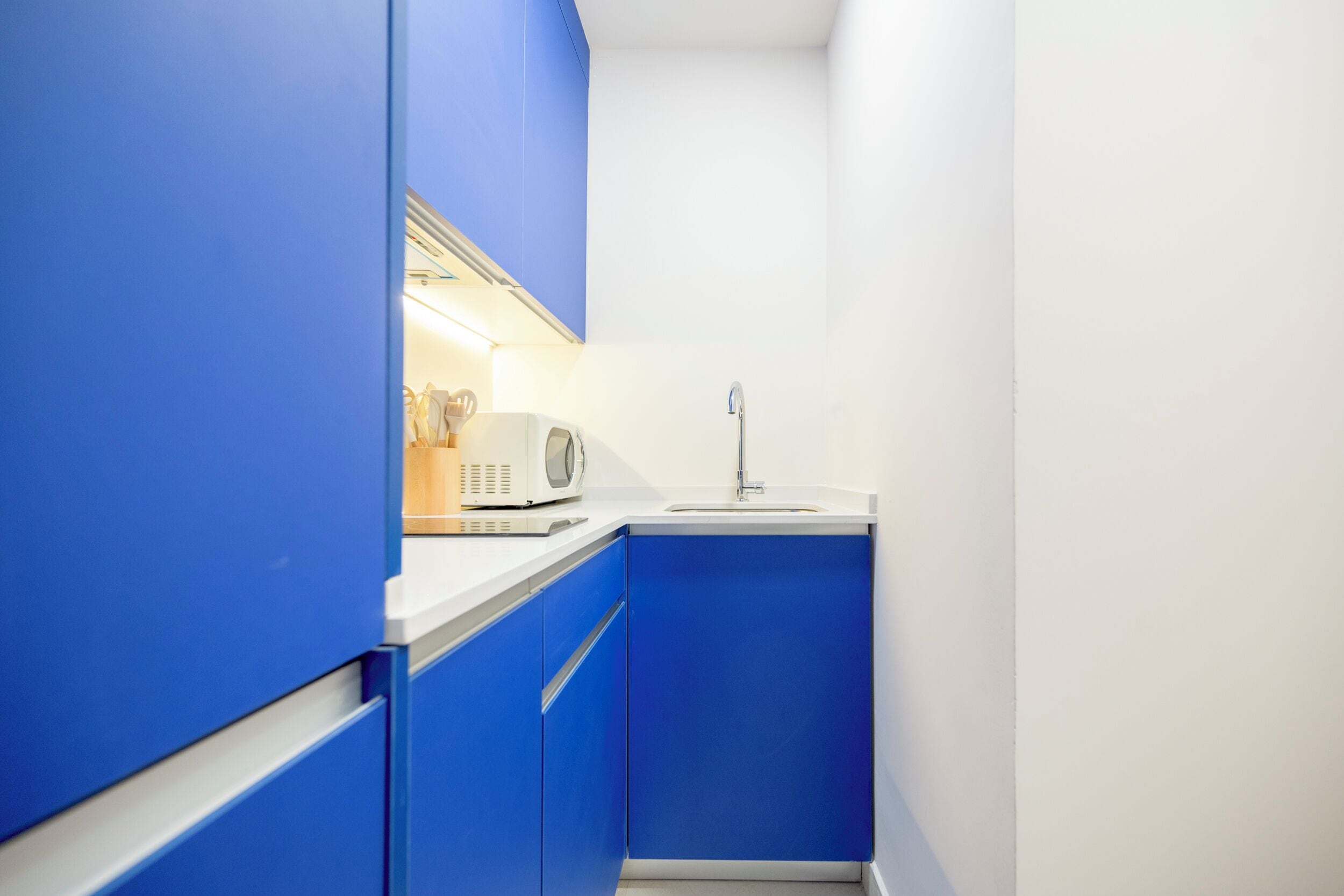 A compact kitchen with blue cabinets, a white countertop, and a microwave.