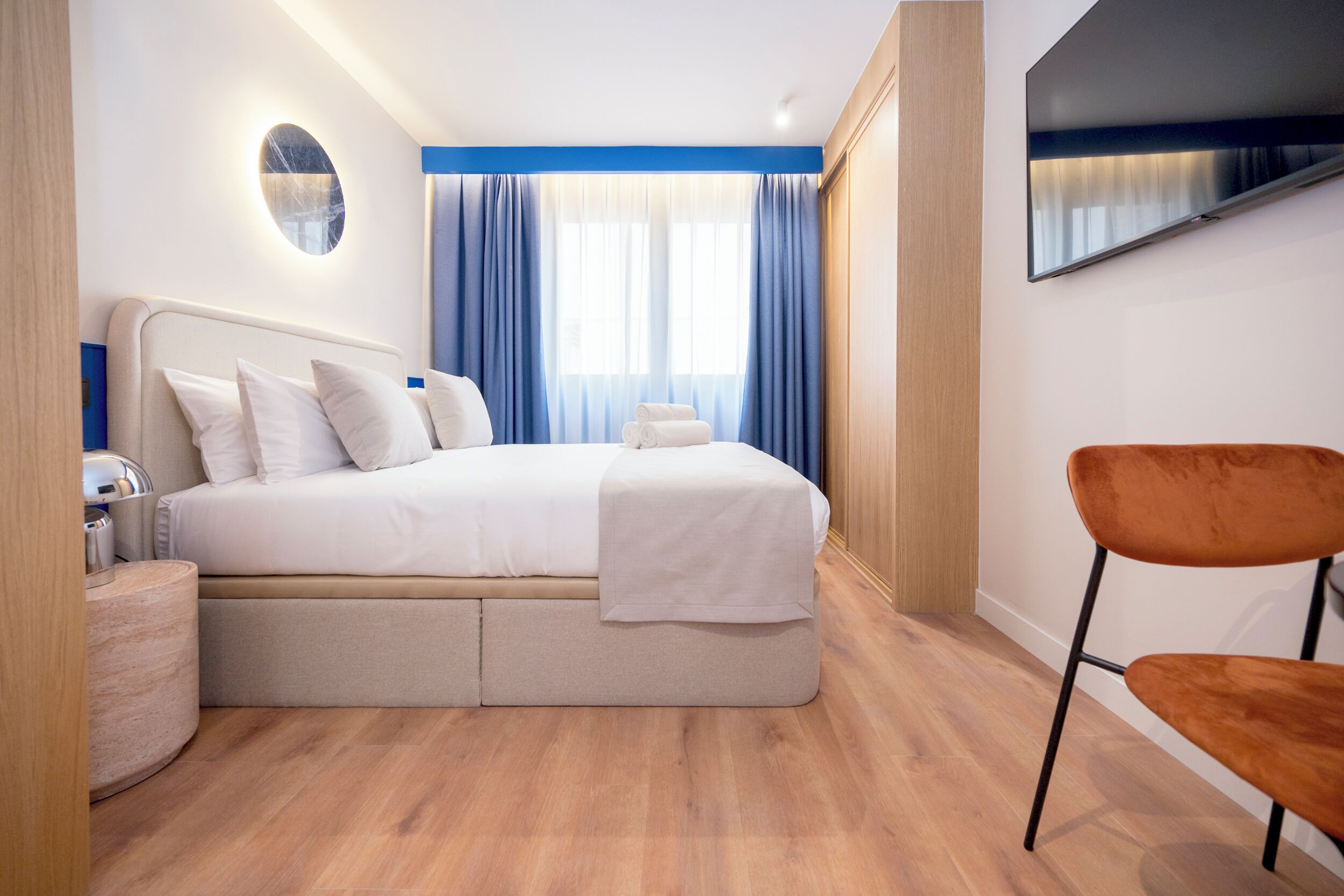 Habitación de hotel moderna con una cama grande, un televisor de pantalla plana, piso de madera y una pared de acento azul.