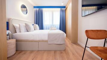 Habitación de hotel moderna con una cama grande, un televisor de pantalla plana, piso de madera y una pared de acento azul.