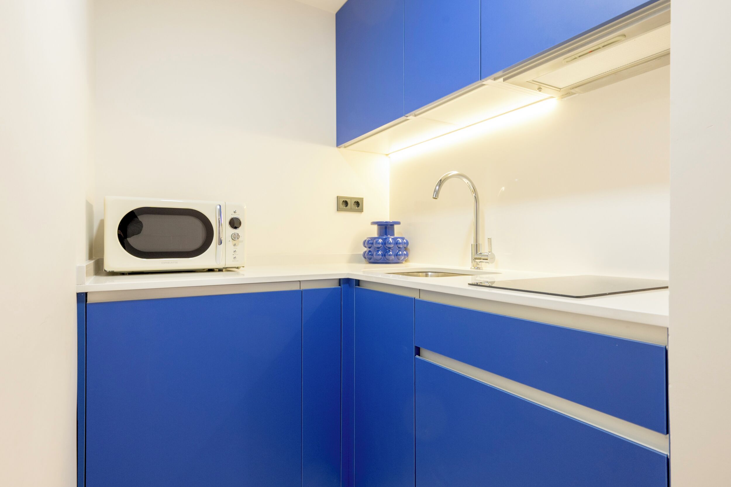 Una cocina con armarios azules, una encimera blanca, microondas, fregadero y grifo.