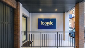Entrada de um hotel com uma placa indicando "iconic SUITES" e um balcão com grades.
