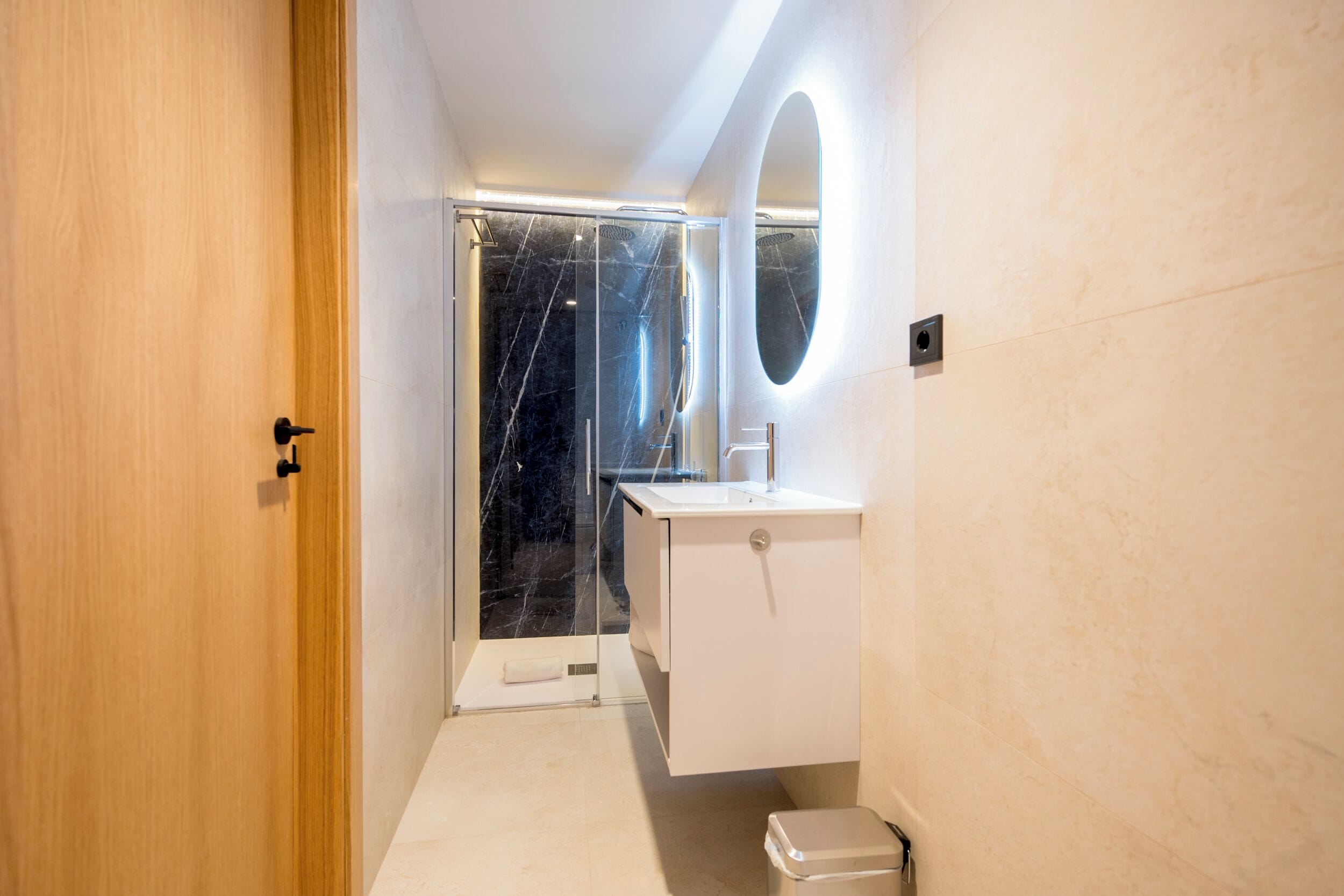 A modern bathroom with a glass shower enclosure, a white sink, and a mirror with an oval frame.