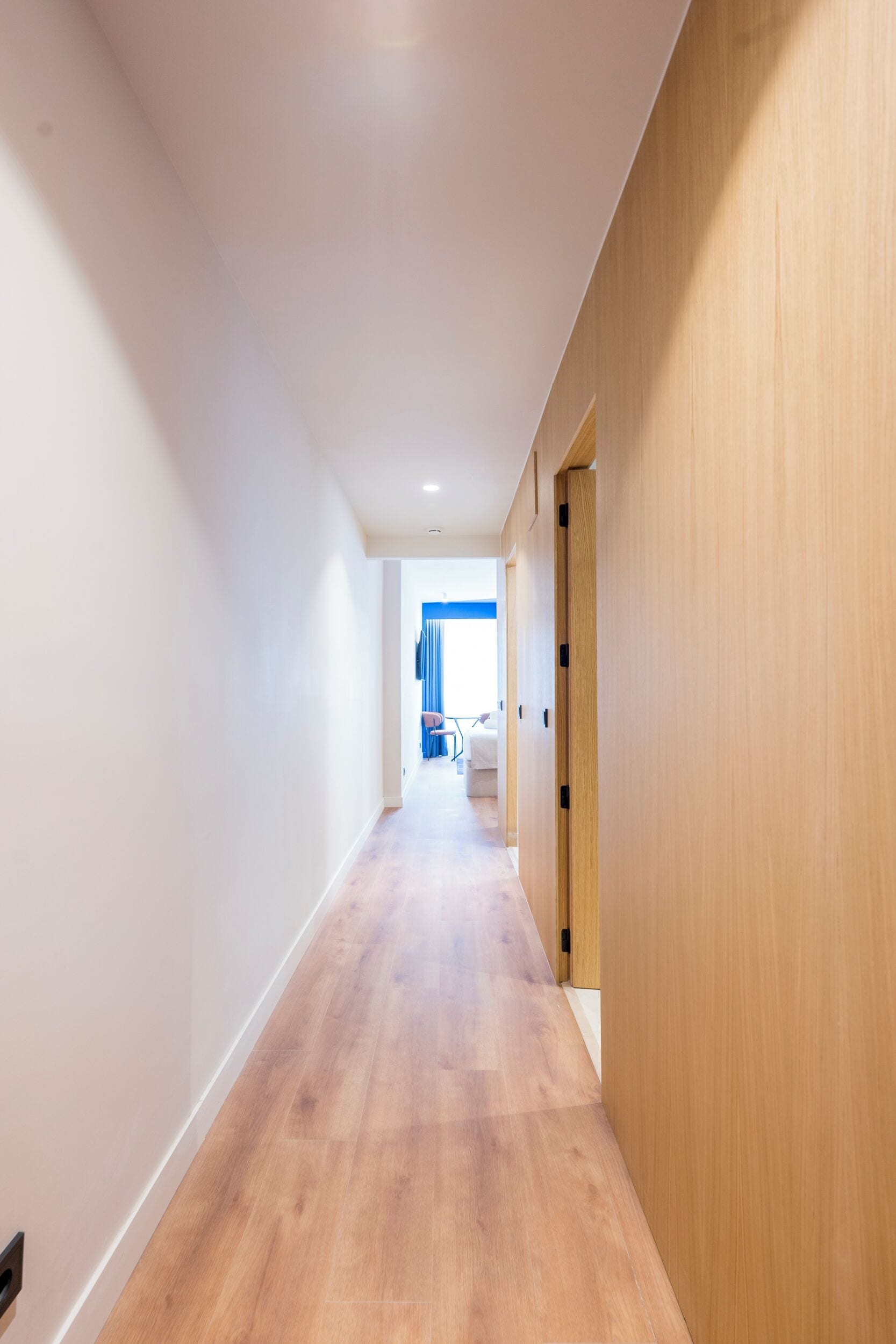 A long, narrow hallway with wooden flooring and white walls.