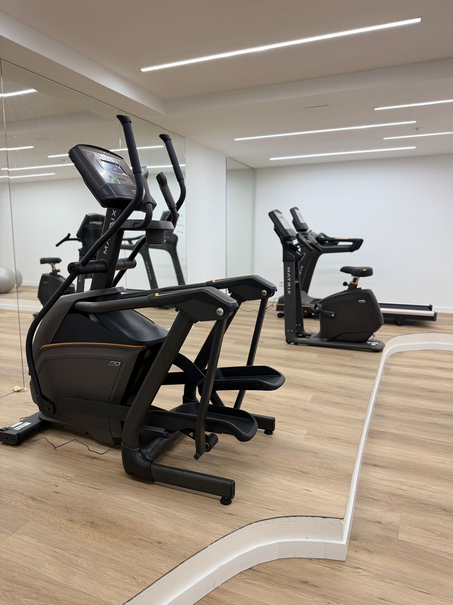 A gym with exercise equipment, a mirror, and a wooden floor.