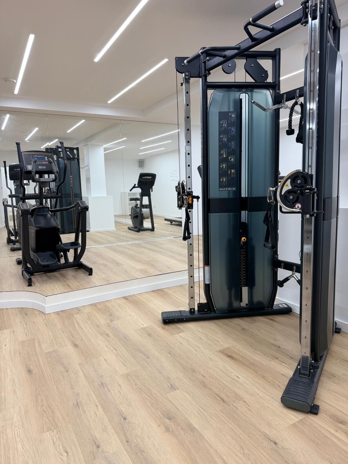 Un gimnasio con equipo de ejercicio, un espejo grande y suelo de madera.