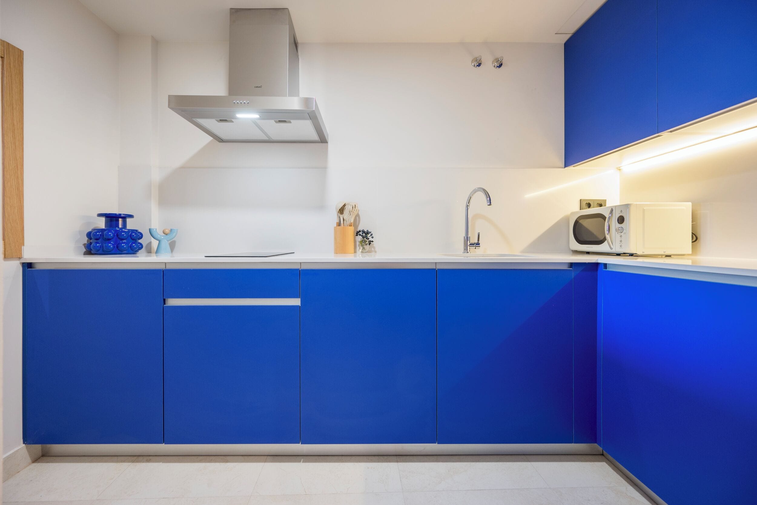 A modern kitchen with blue cabinets, a stainless steel range hood, a microwave, and a sink.