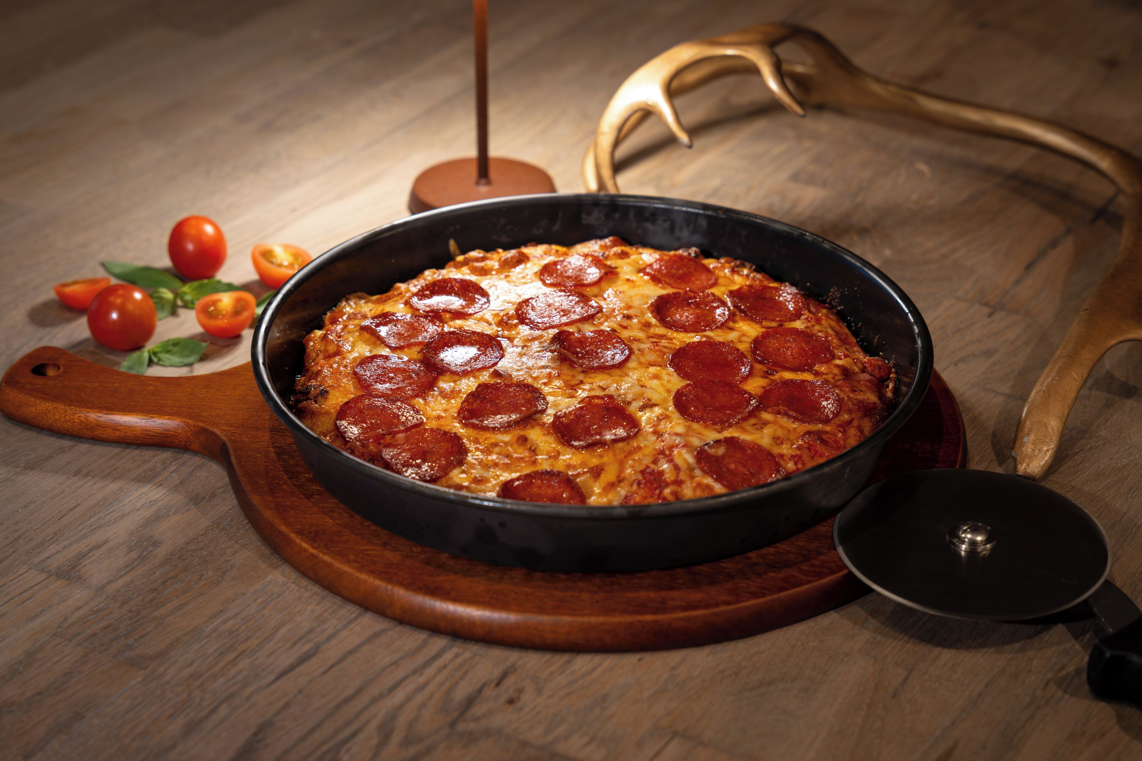 Eine Pepperoni-Pizza in einer schwarzen Bratpfanne auf einem Holzboden.