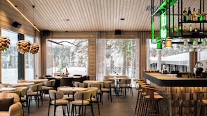 A modern interior with wooden ceiling panels, round tables, and chairs arranged for dining. - Wilderness Hotel Kieppi (Saariselkä)