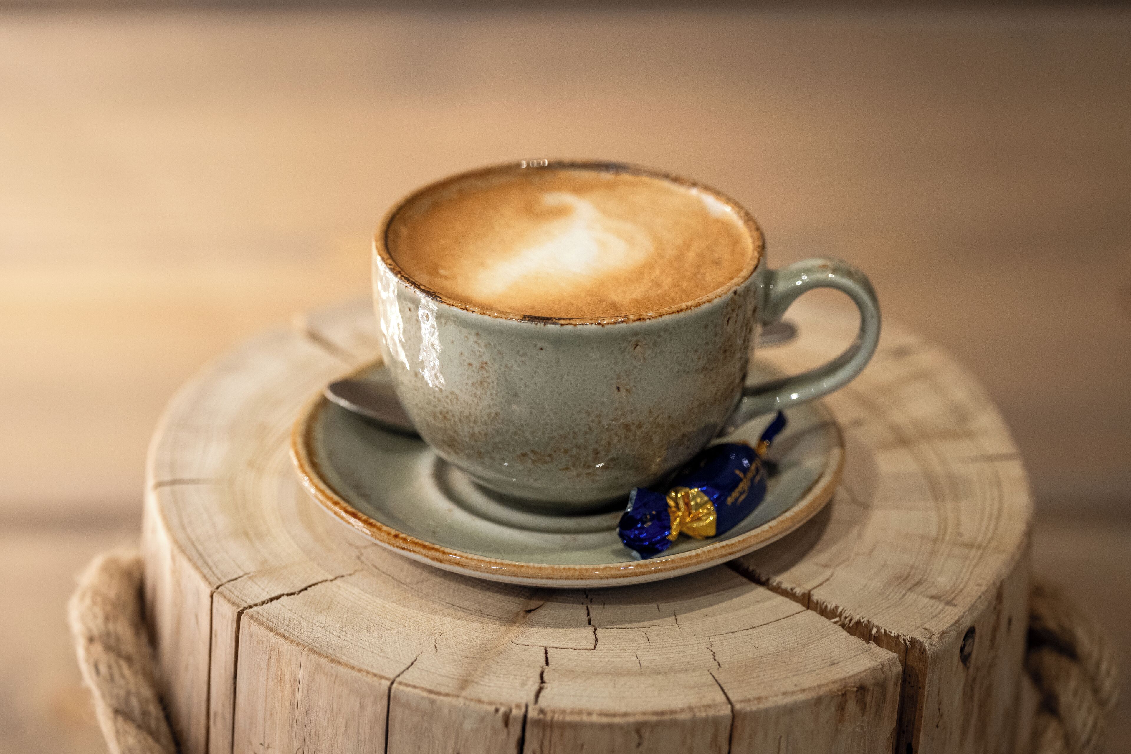 Una taza de café con una figura de corazón en la espuma, sobre un platito, apoyada en un tocón de madera.