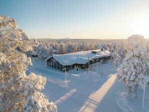 Eine schneebedeckte Lodge mit einem großen Hauptgebäude und kleineren Bauten, umgeben von dichtem Wald.