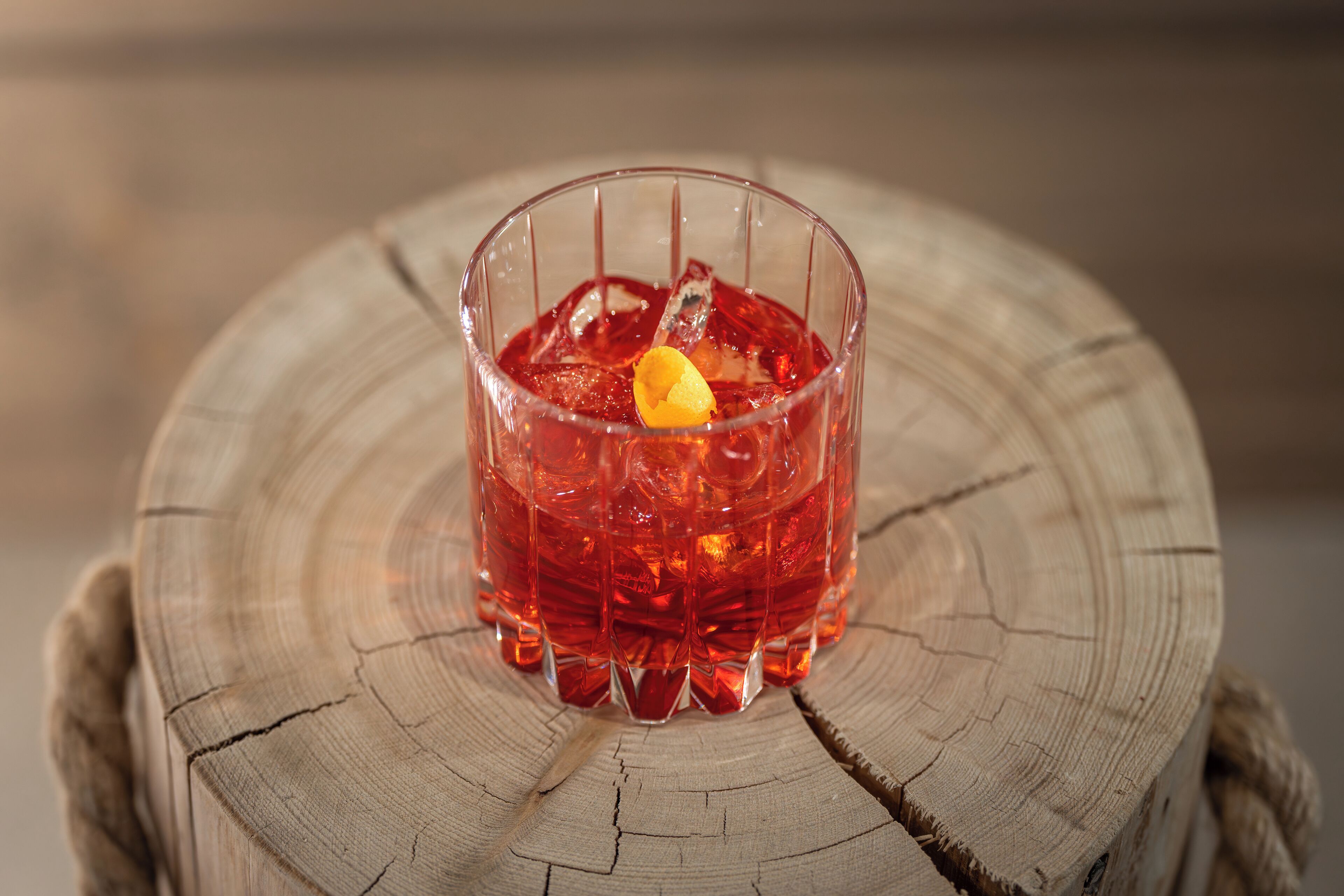 A glass of red beverage with ice cubes and a lemon slice on a wooden surface.