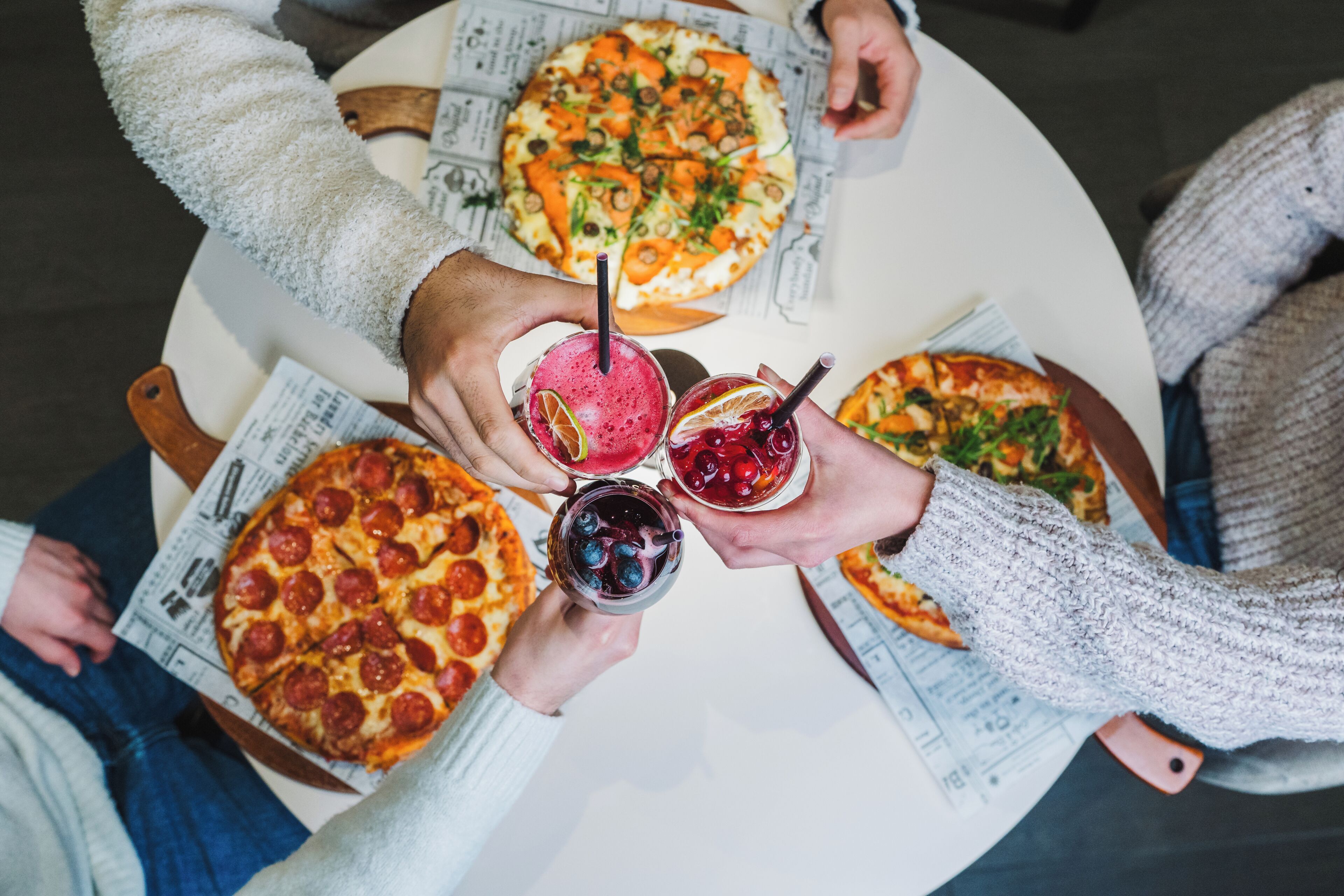 Ein runder Tisch mit Pizza und Getränken, umringt von Menschen.